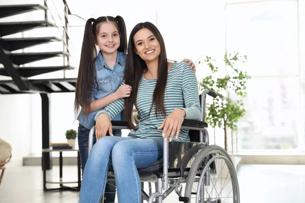 Młoda kobieta na wózku inwalidzkim z córką w pomieszczeniu — Zdjęcie stockowe