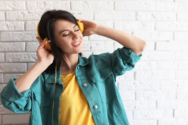 Πορτρέτο της όμορφης γυναίκας ακούγοντας μουσική με ακουστικά κοντά σε τοίχο τούβλο — Φωτογραφία Αρχείου