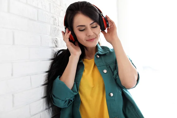 Porträt einer schönen Frau, die Musik mit Kopfhörern in der Nähe von Ziegelmauer hört — Stockfoto