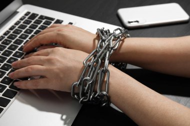 Siyah arka planda dizüstü bilgisayar kullanan elleri zincirli bir kadın, yakın plan. Yalnızlık kavramı