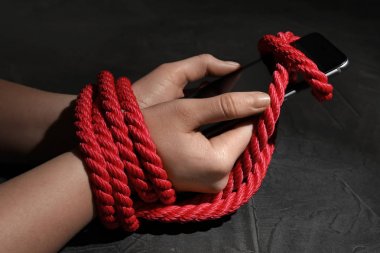İpli elleri olan bir kadın gri arka planda akıllı telefonu tutuyor, yakın plan. Yalnızlık kavramı