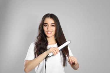 Gri arka planda saç demiri kullanan mutlu kadın