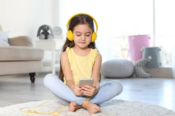 Criança bonito com fones de ouvido e telefone celular no chão dentro de casa — Fotografia de Stock