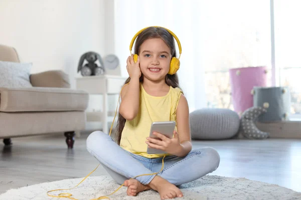 Criança bonito com fones de ouvido e telefone celular no chão dentro de casa — Fotografia de Stock