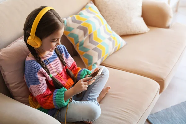 Lindo niño con auriculares y teléfono móvil en el sofá interior. Espacio para texto —  Fotos de Stock