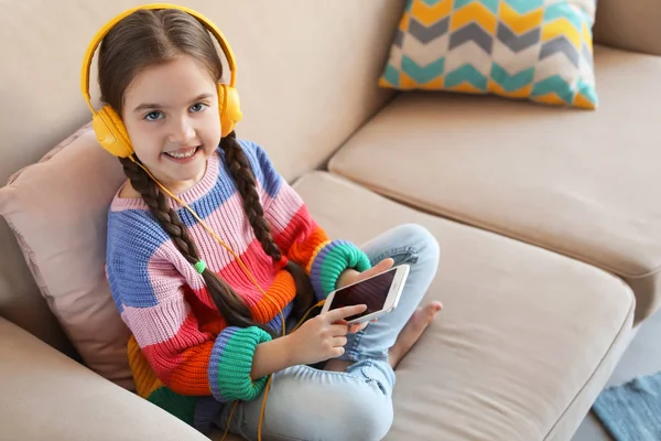 Schattig kind met een koptelefoon en mobiele telefoon op de sofa binnenshuis. Ruimte voor tekst — Stockfoto