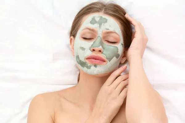 Belle femme avec masque facial en argile sur tissu blanc, vue ci-dessus — Photo