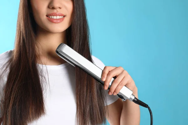 Mujer feliz usando plancha para el cabello sobre fondo de color, primer plano — Foto de Stock