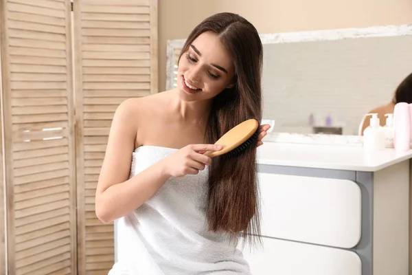 Красивая улыбающаяся молодая женщина с расчёской в ванной комнате — стоковое фото