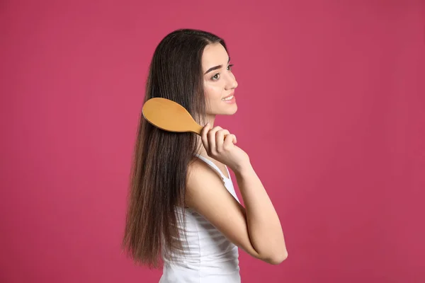 Hermosa joven sonriente con cepillo de pelo sobre fondo de color — Foto de Stock