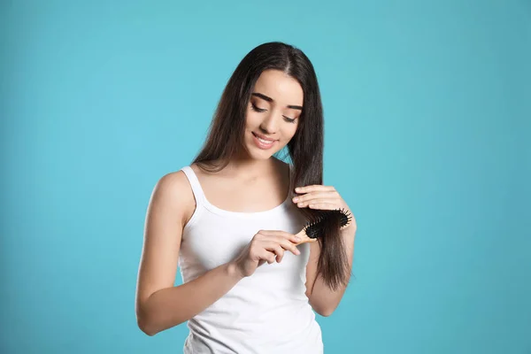 Hermosa mujer joven con cepillo de pelo sobre fondo de color — Foto de Stock