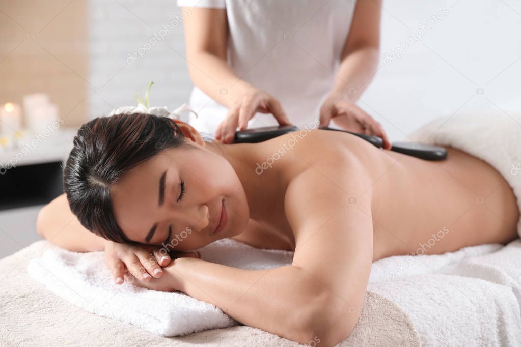Beautiful Asian woman getting hot stone massage in spa salon