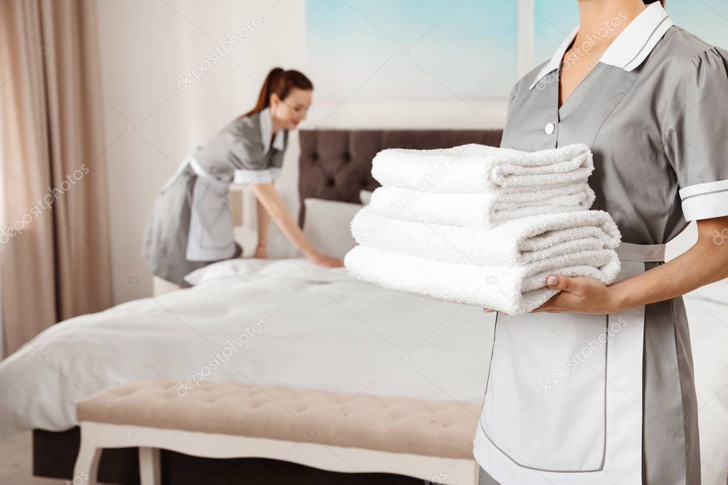 Chambermaid with stack of fresh towels in hotel room, closeup. Space for text
