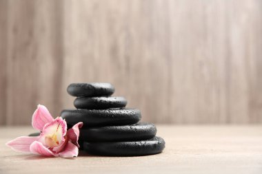 Ahşap arka plan üzerinde çiçek ile siyah spa taşları yığını. Metin için alan