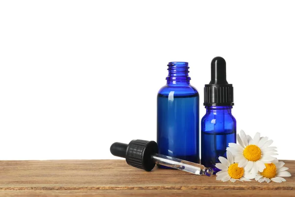 Kamille bloemen en cosmetische flessen etherische olie op houten tafel tegen witte achtergrond. Ruimte voor tekst — Stockfoto