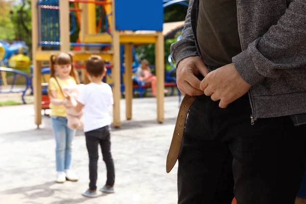 Sospechoso hombre adulto quitándose los pantalones en el patio de recreo con niños pequeños, espacio para el texto. Niño en peligro —  Fotos de Stock