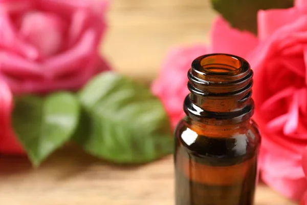 Open bottle of rose essential oil on table, space for text