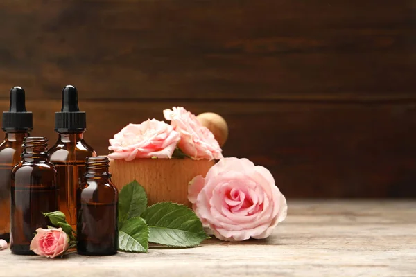 Butelki z róży olejku i kwiatów na drewnianym stole, miejsce na tekst — Zdjęcie stockowe