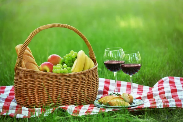 Cesta de vime com comida e vinho em cobertor no parque. Piquenique de verão — Fotografia de Stock