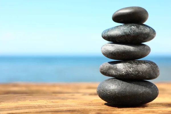 Montón de piedras en la mesa de madera contra el paisaje marino, espacio para el texto. Concepto zen — Foto de Stock