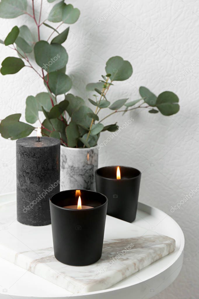 Burning candles and green branches on table at white wall, space for text