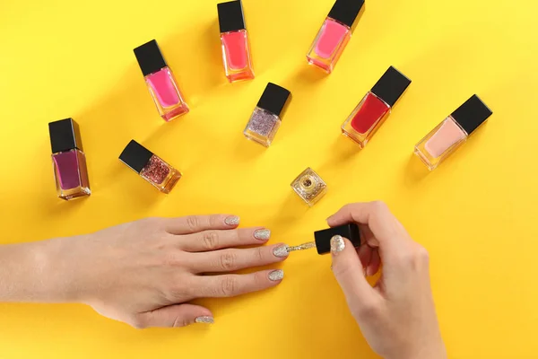 Mujer aplicando esmalte de uñas sobre fondo de color, vista superior — Foto de Stock