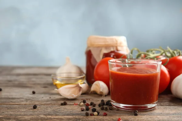 Samenstelling met glas smakelijke tomatensaus op houten tafel tegen kleur achtergrond. Ruimte voor tekst — Stockfoto