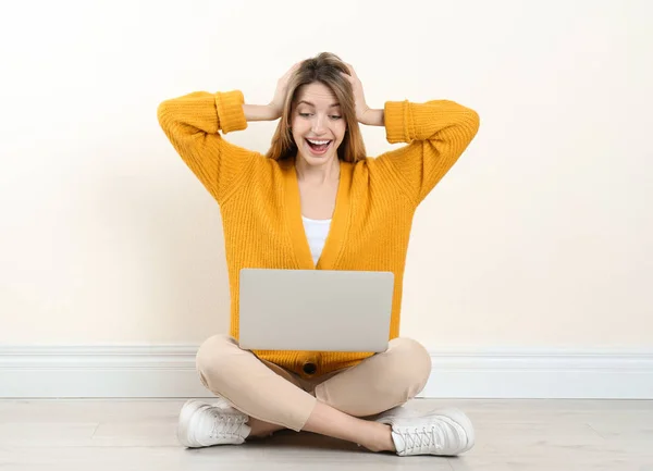 Surprise jeune femme avec ordinateur portable assis sur le sol près du mur de lumière à l'intérieur — Photo