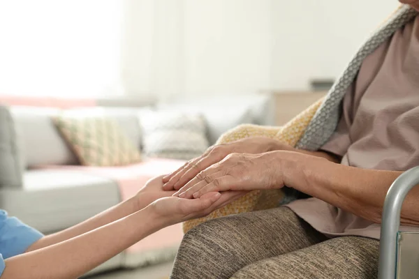 Enfermeira segurando as mãos da mulher idosa dentro de casa, fechar com espaço para texto. Assistência aos idosos — Fotografia de Stock