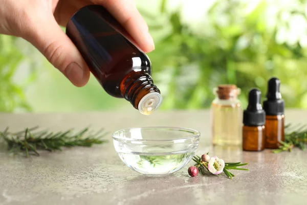 Mujer goteando aceite de árbol de té natural en un tazón sobre un fondo borroso, primer plano — Foto de Stock