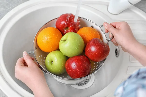 Woman washing fresh fruits in colander under water, closeup