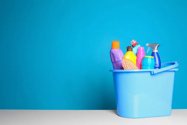 Balde de plástico com diferentes produtos de limpeza na mesa contra fundo de cor. Espaço para texto — Fotografia de Stock