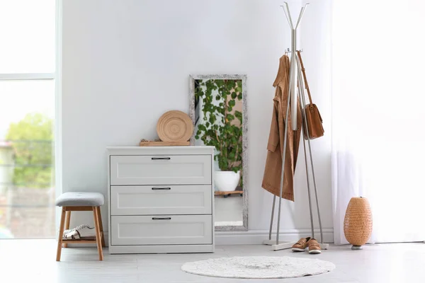 Modern hallway interior with chest of drawers and clothes on hanger stand