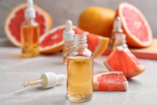 Flaskor med eterisk olja och färska grapefrukter på grått bord — Stockfoto