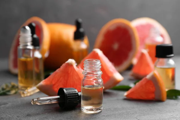 Flaskor av eterisk olja och grapefrukter på grått bord — Stockfoto