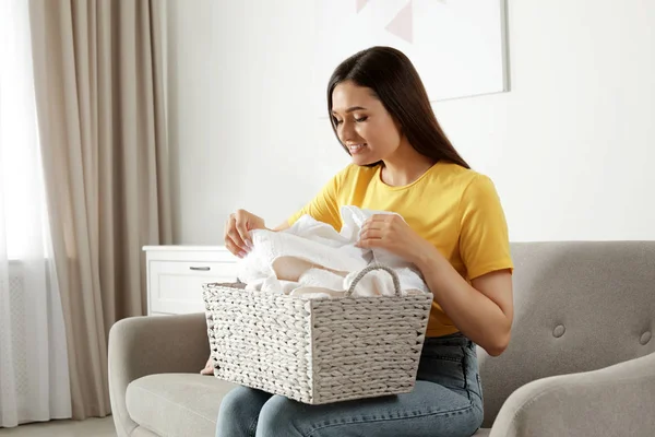 Jonge vrouw met wasmand vol schone handdoeken op de bank binnen — Stockfoto