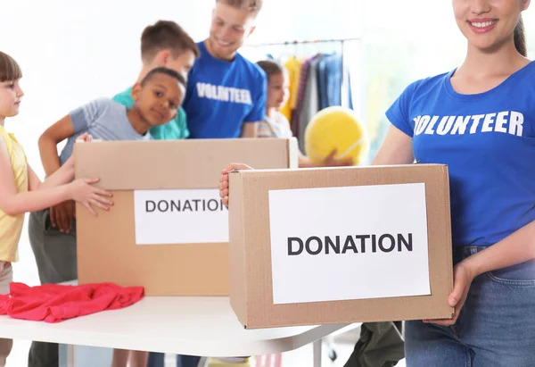 Voluntarios con niños clasificando bienes de donación en interiores — Foto de Stock