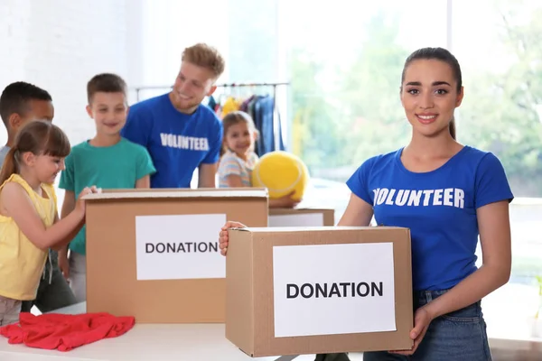 Vrijwilligers met kinderen die donatie goederen binnenshuis sorteren — Stockfoto