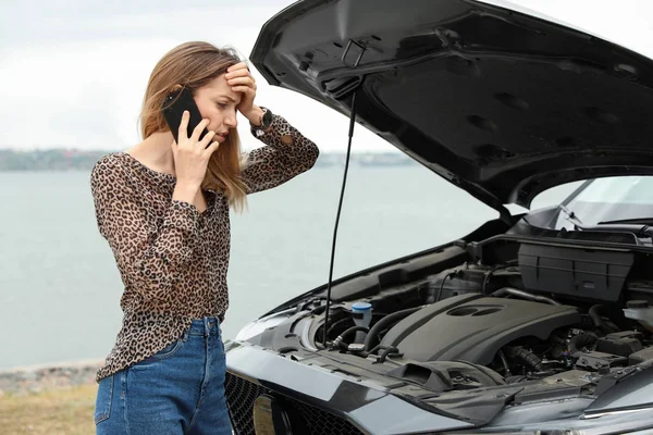 Zavaros fiatal nő beszél a telefon közelében törött autó a szabadban — Stock Fotó