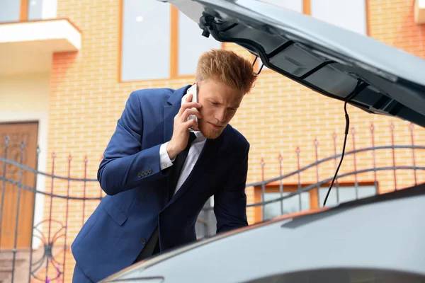 Zavaros fiatal üzletember beszél a telefon közelében törött autó a szabadban — Stock Fotó