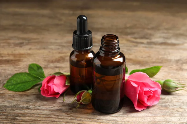 Butelki z róży olejek Eterowy i kwiaty na drewnianym stole — Zdjęcie stockowe
