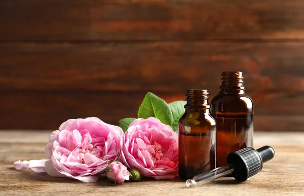 Бутылки розового эфирного масла, пипетки и цветы на деревянном столе. Пространство для текста — стоковое фото