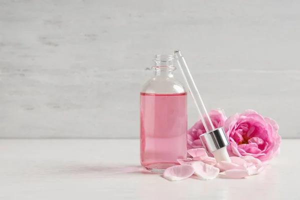 Fresh flowers, bottle of rose essential oil and pipette on table, space for text
