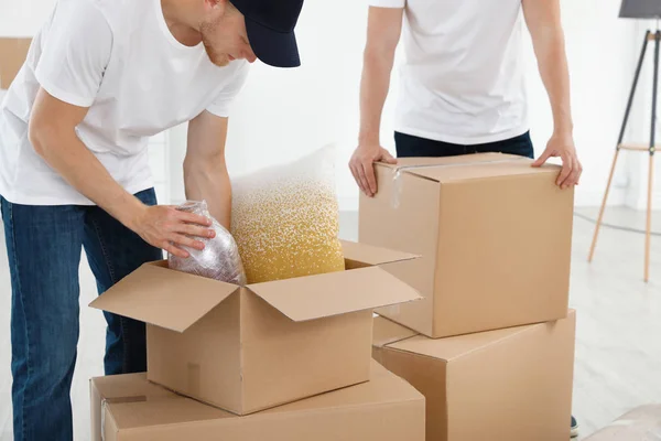 Moving service employees with cardboard boxes and belongings in room, closeup