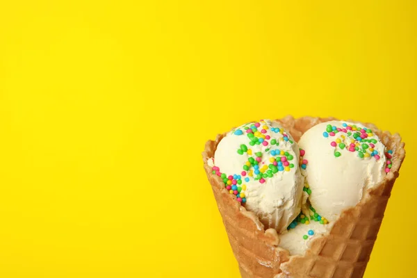 Delicious ice cream with sprinkles in waffle cone on color background, space for text