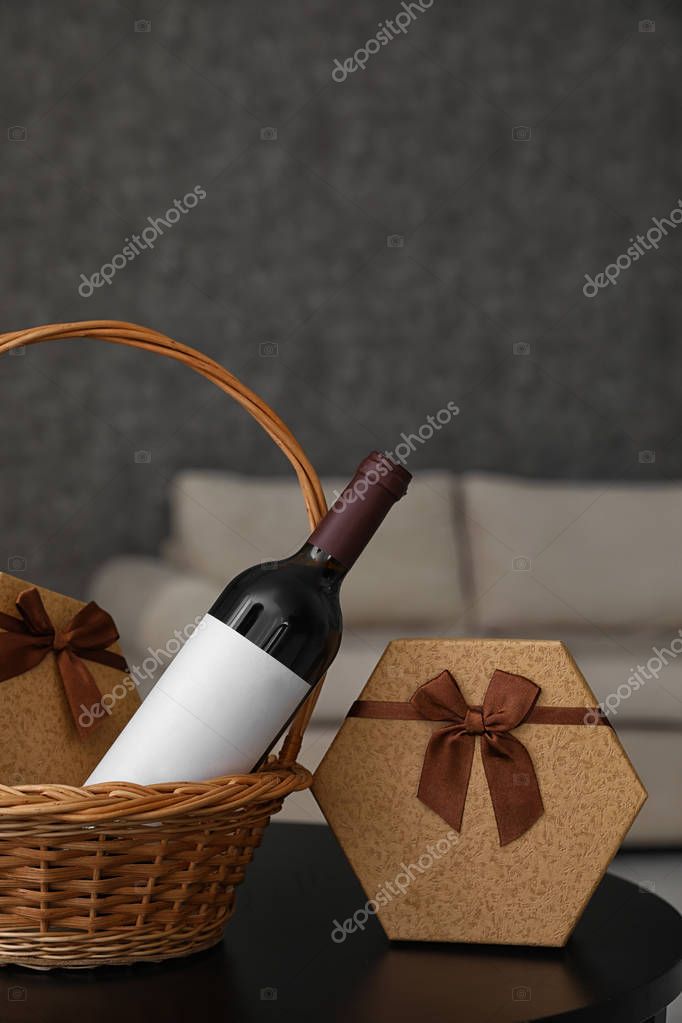 Wicker basket with bottle of wine and gift boxes on table in room. Space for design