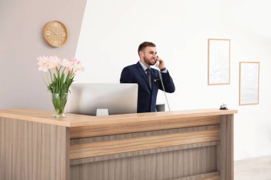 Resepsiyonist modern otelde masada telefonda konuşuyor