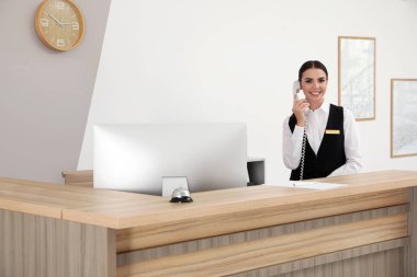 Resepsiyonist modern otelde masa yakınında telefonla konuşuyor