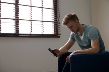 Kapalı pencere yakınında koltukta cep telefonu ile Yalnız adam