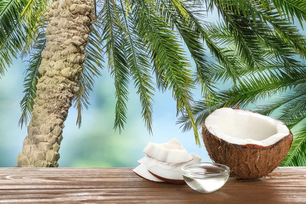 Kokos en natuurlijke organische olie op houten tafel tegen tropische palmbladeren — Stockfoto